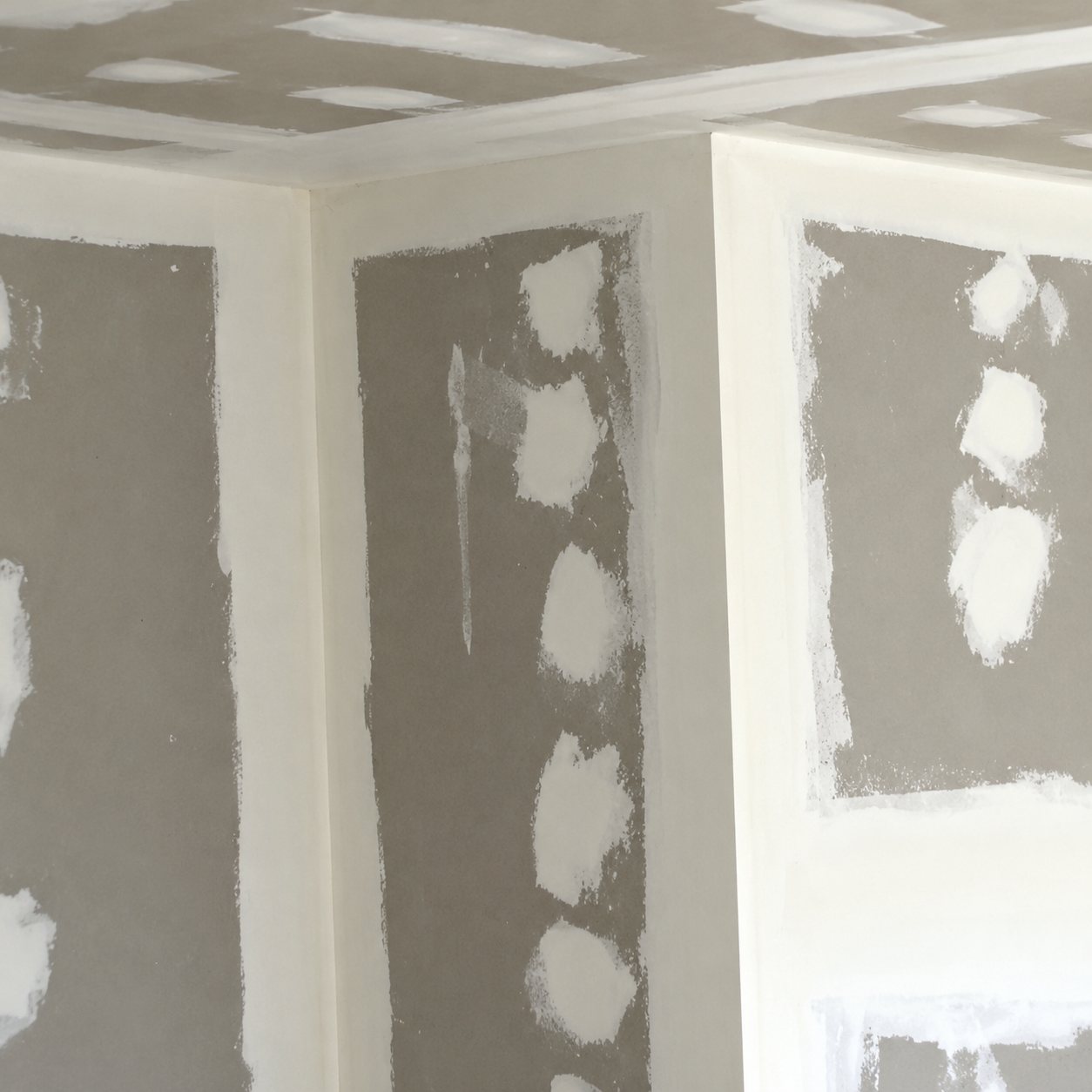 Gros plan sur des cloisons en plaques de plâtre avec des traces d'enduit aux joints et aux vis, dans un chantier de rénovation intérieure.