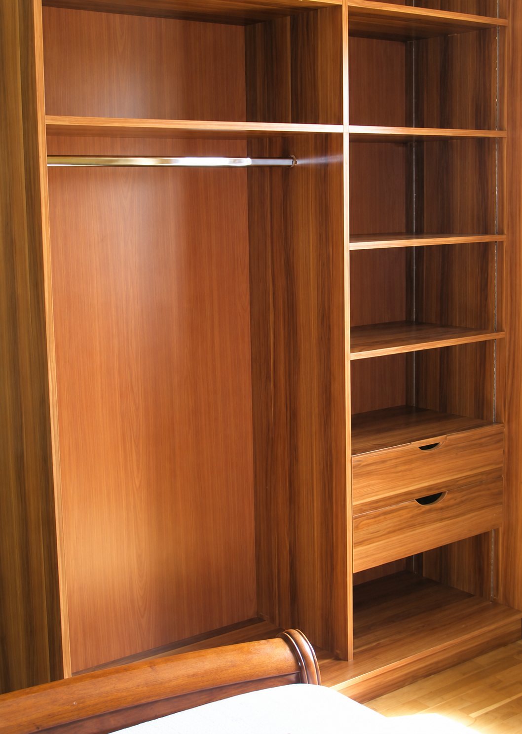 Un dressing en bois d'aspect acajou avec une penderie, des étagères et deux tiroirs, installé dans une chambre près d'un lit.