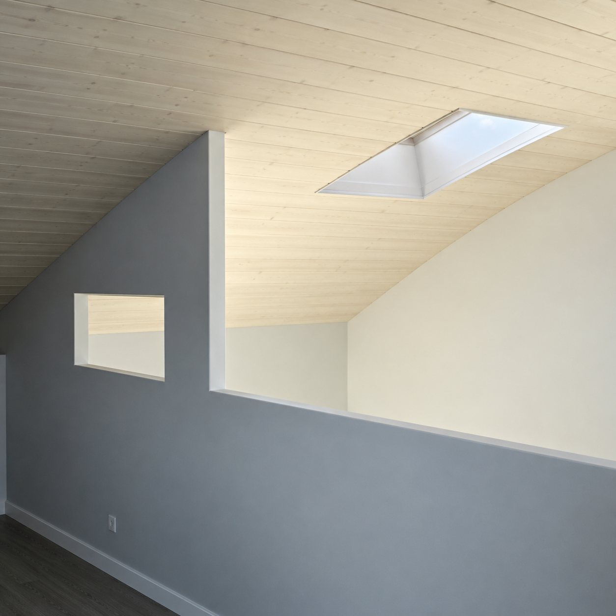 Pièce sous les combles aux murs clairs, éclairée par une fenêtre de toit qui projette des taches de lumière sur la paroi.